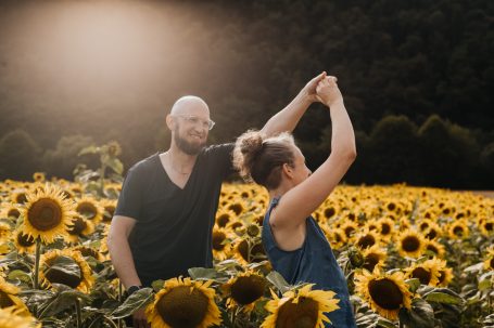 Paar tanzt glücklich in einem Sonnenblumenfeld bei Sonnenlicht.