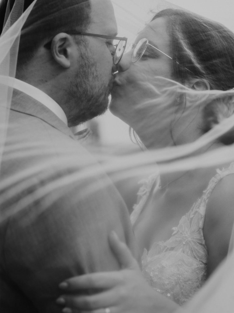 Ein Brautpaar küsst sich liebevoll, umgeben von sanftem Schleier.