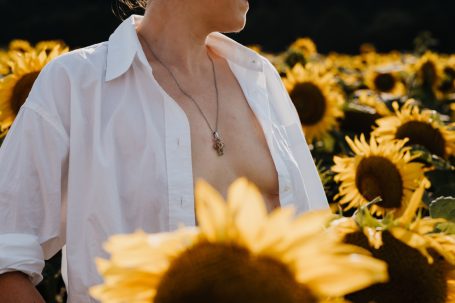 Person in weißen Hemd steht zwischen Sonnenblumenfeld, der Blick ist nach rechts gerichtet.