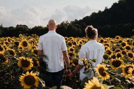 Paar in weißen Hemden, Hand in Hand in einem Sonnenblumenfeld stehend.