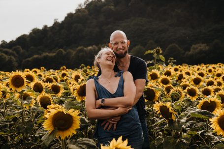 Ein Paar lacht und umarmt sich in einem Sonnenblumenfeld.